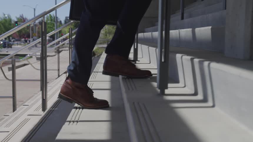 Businessman wearing a suit and carrying a suitcase goes up the stairs to the office building