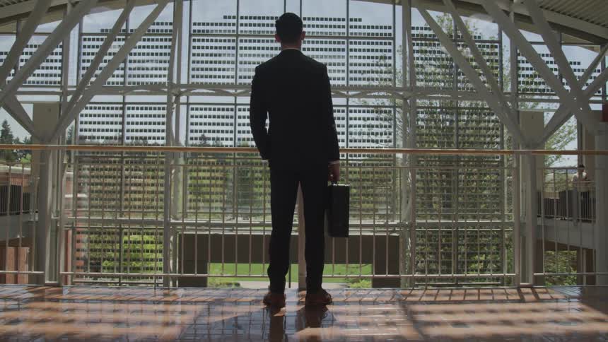 Businessman holding briefcase standing on elevated walkway looking at the outdoors through grated panels