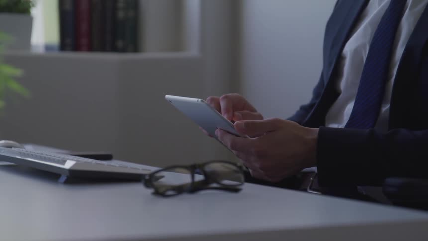 Man in business suit sits at desk and uses tablet