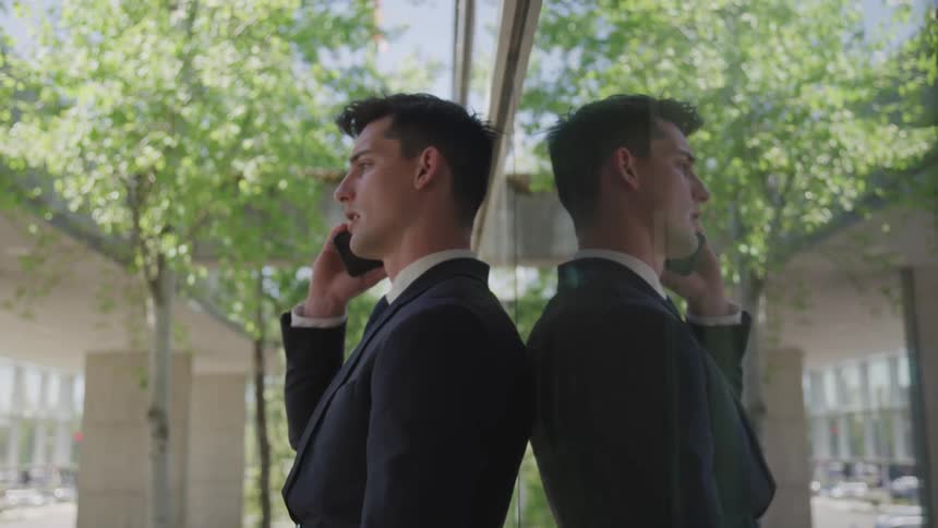 A young man leans against a wall and talks on his cell phone