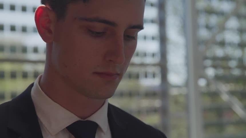 A man in an office wearing a suit stands near a window then looks up
