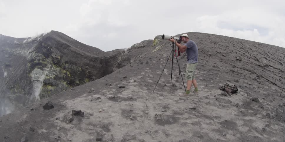 A man in a blue shirt taking pictures on a mountain