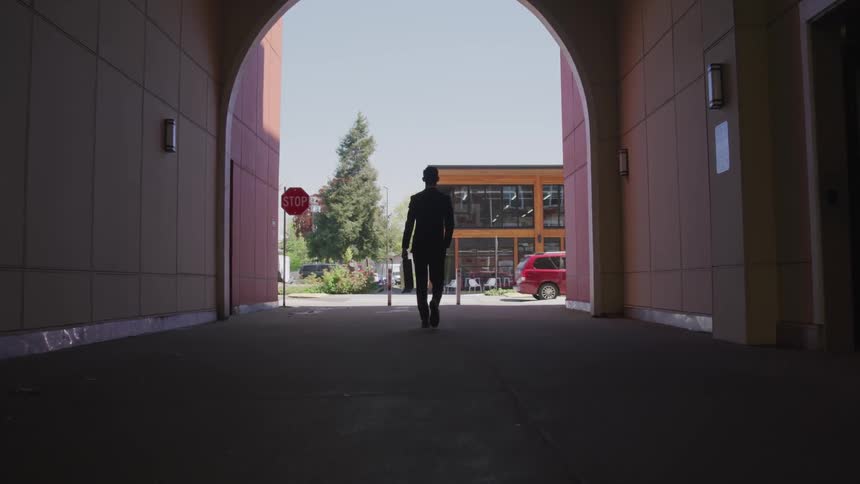 A man carrying a briefcase walks through an arch covered walkway towards the street