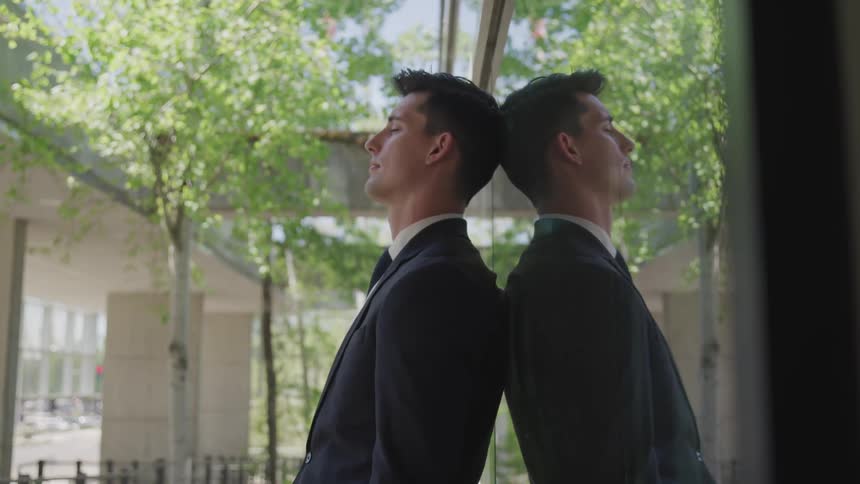 Business man wearing a suit leans against window in front of the office building