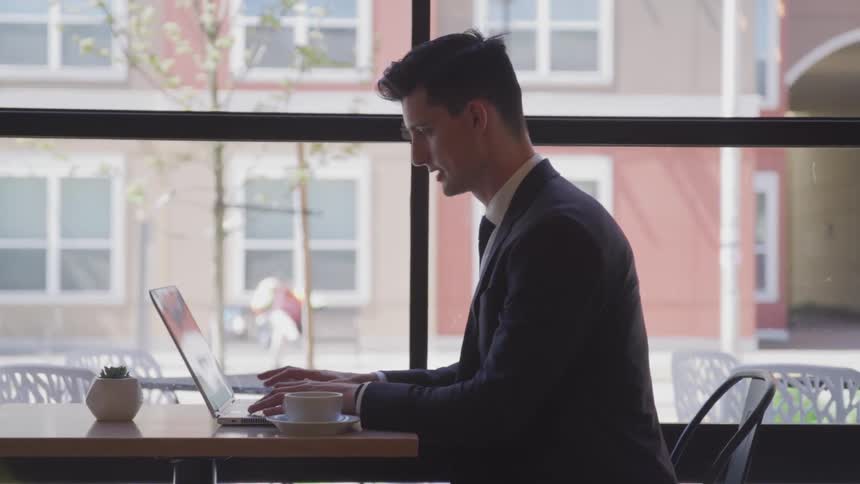 A man types on his laptop in a coffee shop