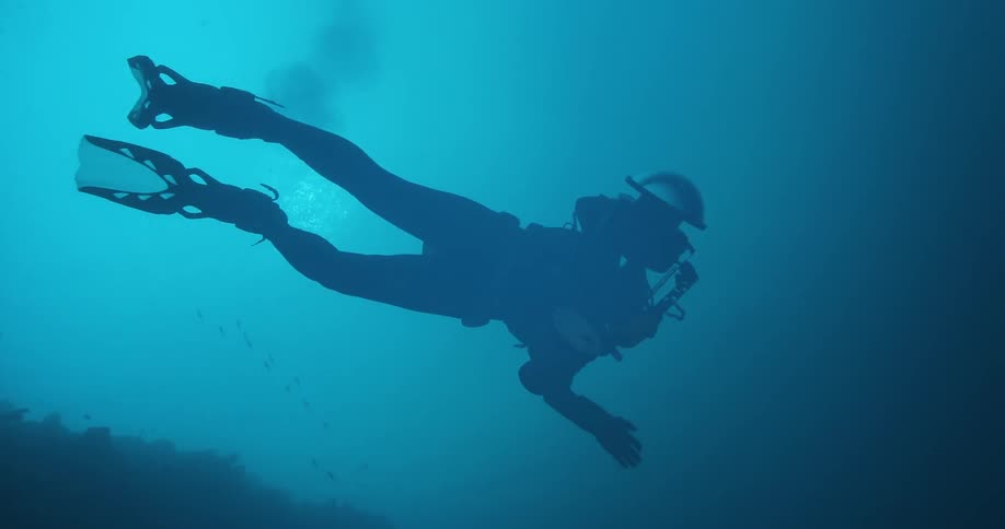 A scuba diver swims under water while holding equipment