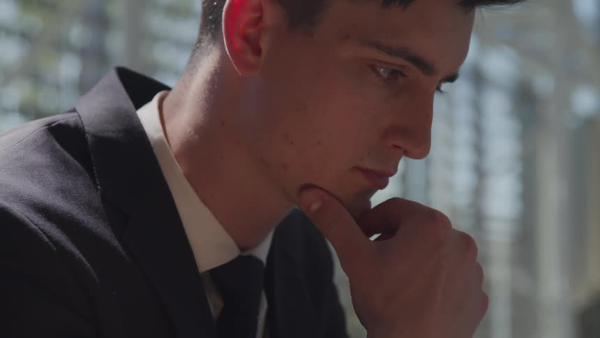 Sad man sitting outdoors with hand on his chin