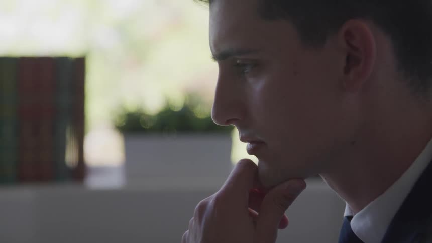 A white male sits with this chin in his hand in an office