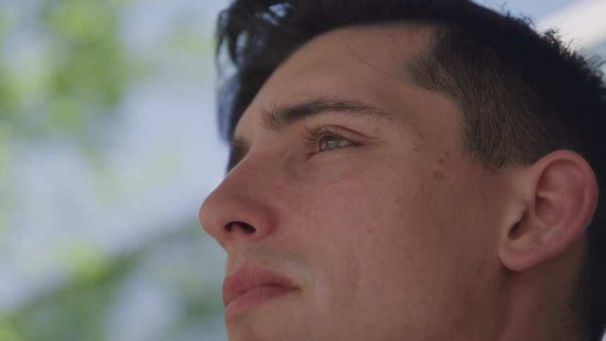 A white man stands outdoors and looks off into the distance