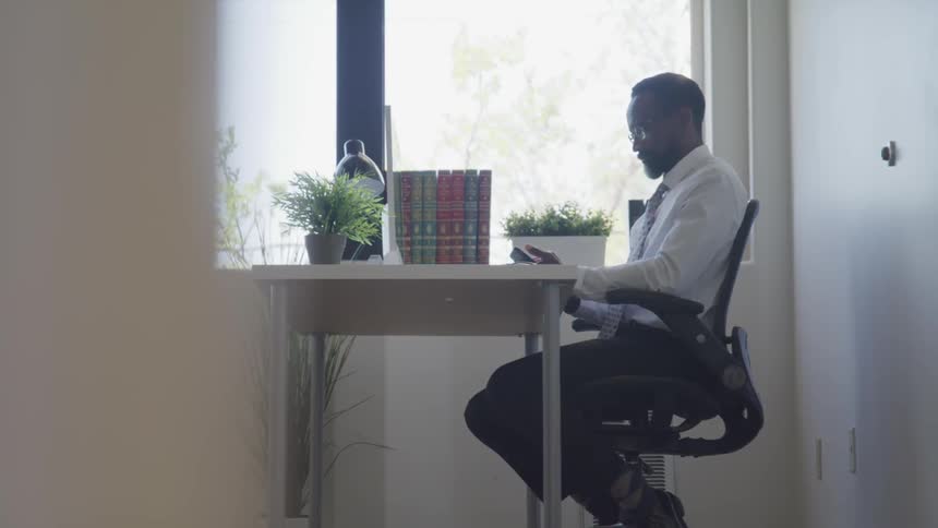 Black businessman sitting at the desk uses the smartphone in the office