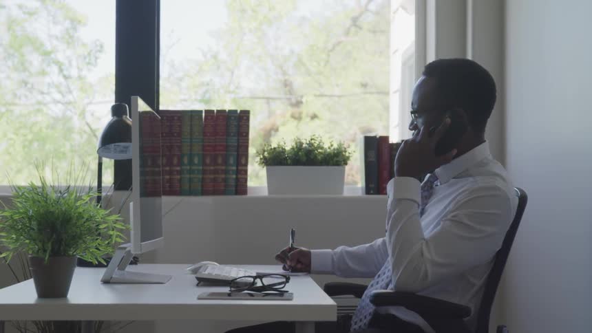 A man sits at his desk on the phone