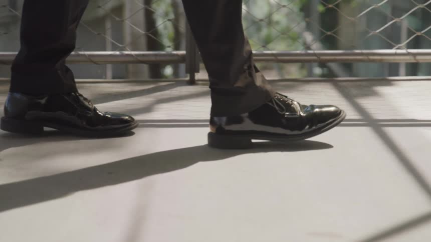 A man in shiny black shoes walks on a walkway