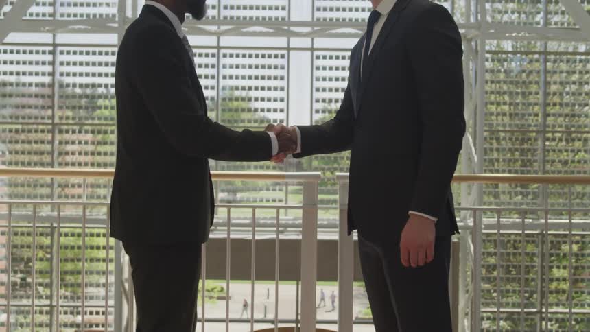 Two men wearing suits shake hands in a building