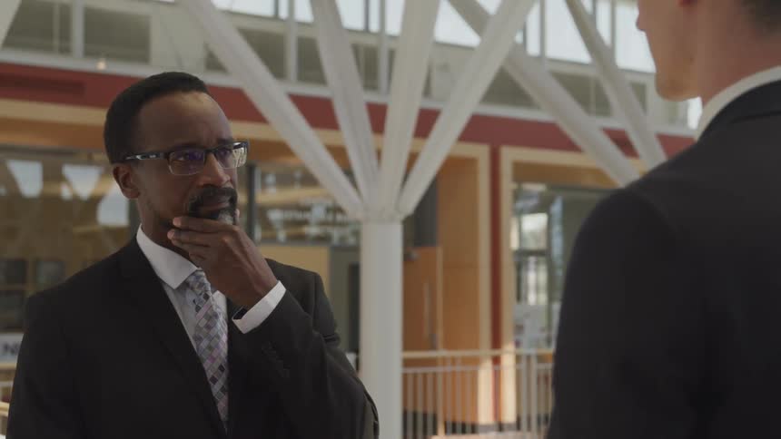 Two men stand inside a building and talk
