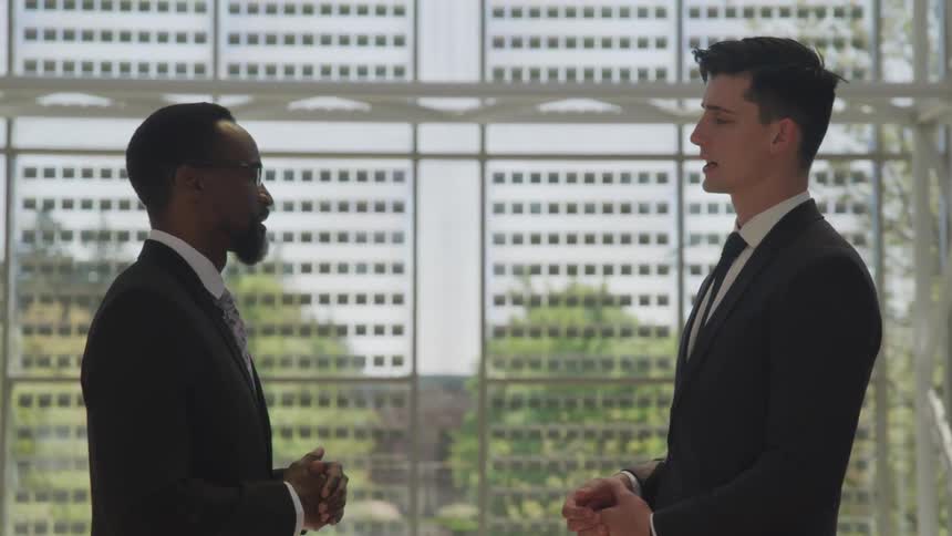 Two men in business suits chat near a window