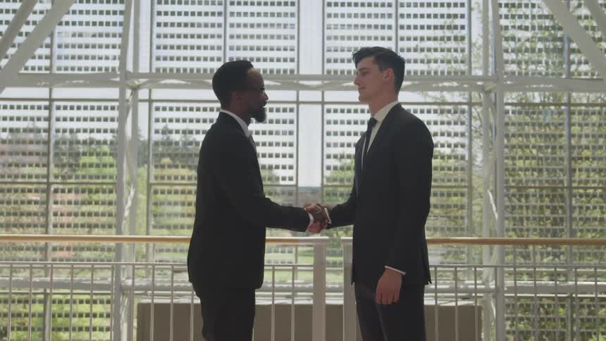 Two men shake hands by the railing
