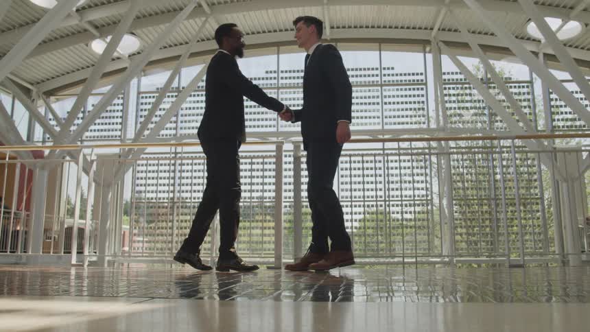 Two men walk across a lobby to each other and shake hands