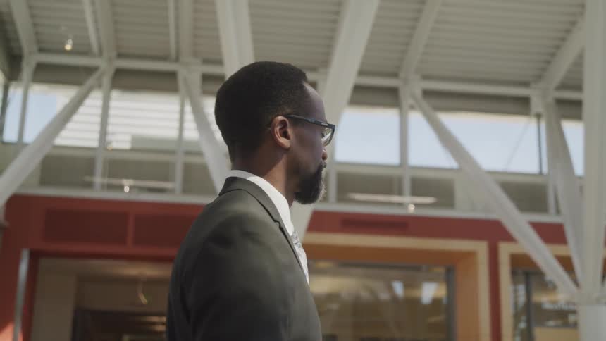 A black man stands in an office building and looks off in to the distance