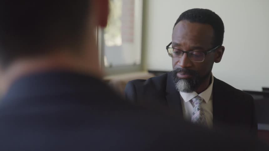 Black and white businessmen sitting at the table look at each other and have a conversation in the office
