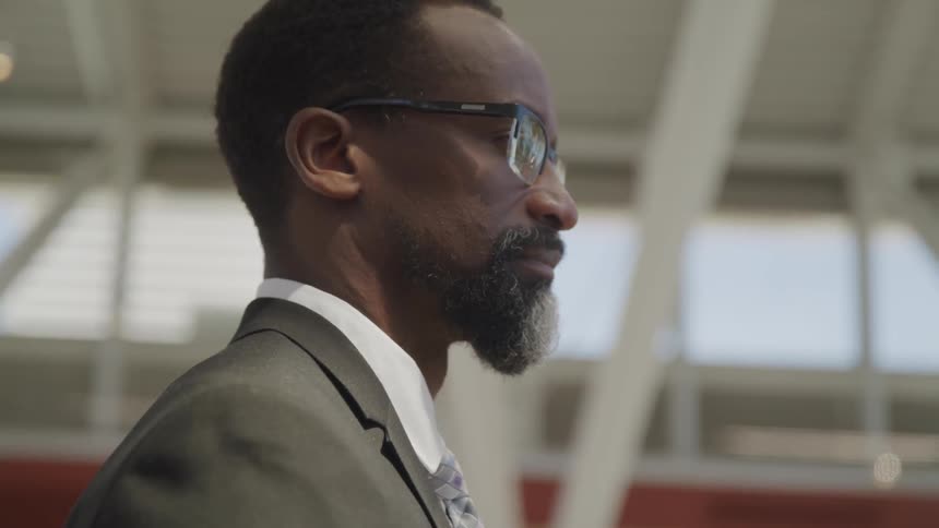 A black man in a suit stares straight ahead of him