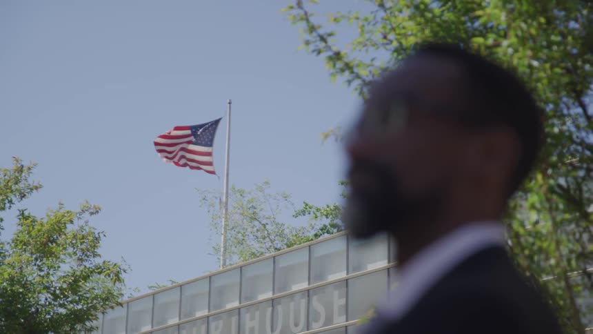 A man stands near a building with an american flag flying on top