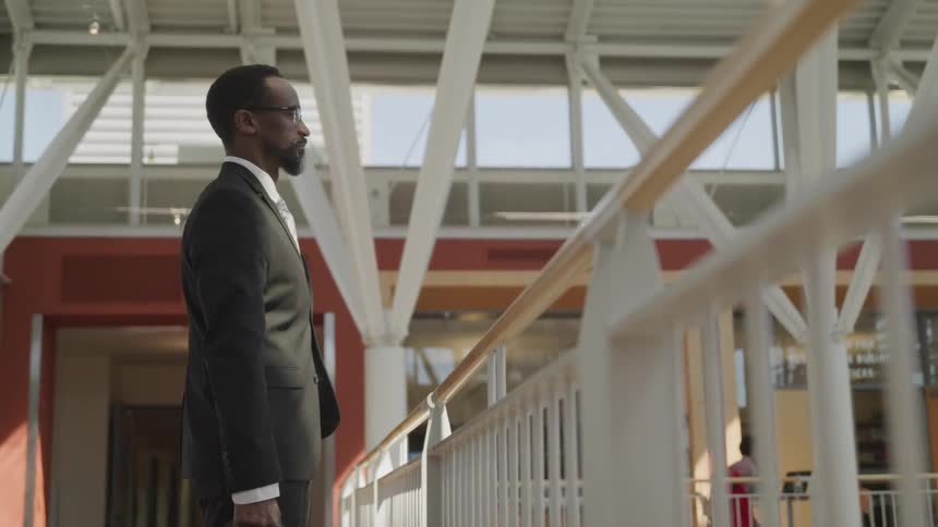 A black man with suit and glasses stand in the rail
