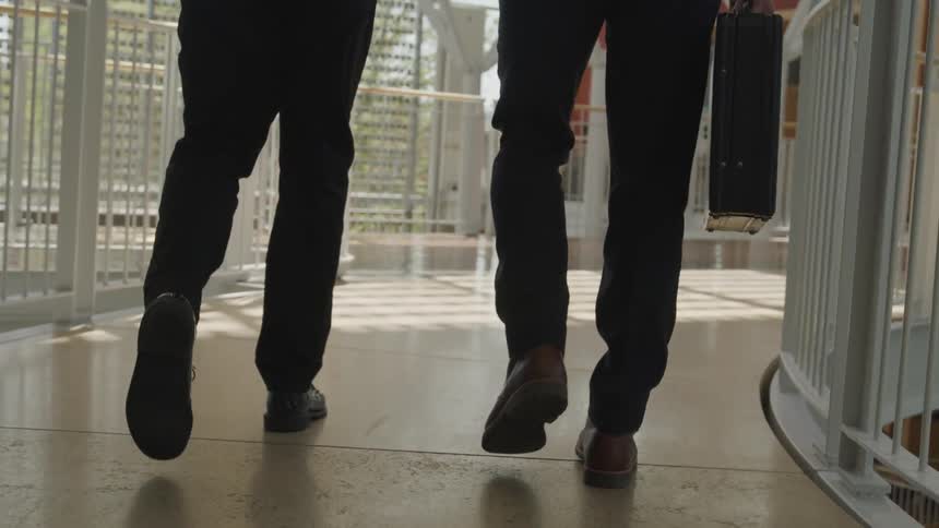 A man carrying a briefcase walks beside a colleague along an elevated walkway