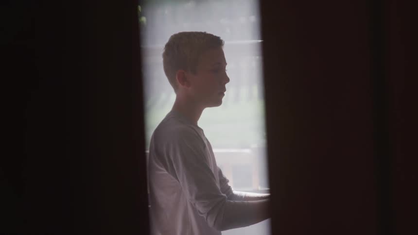 A boy is seen playing the piano through a set of curtains