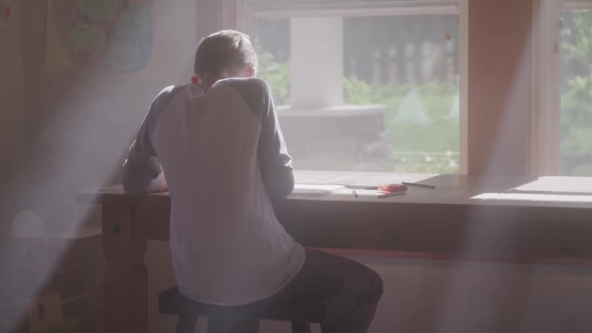 A person sitting down by a desk next to a window