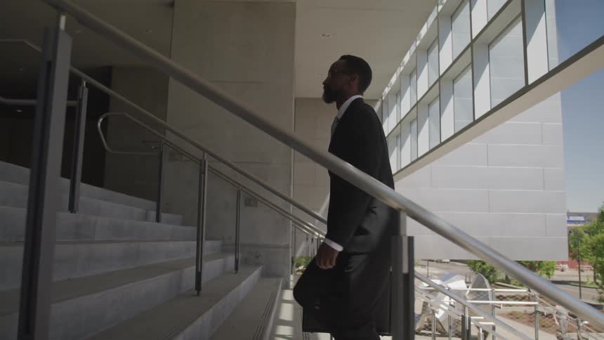 Black business man carrying a brief case walking up stairs into a building