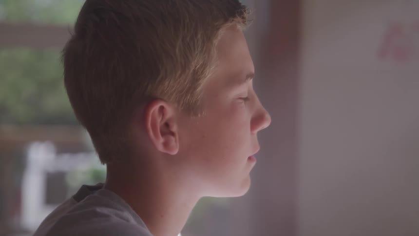 A young male sits indoors while looking forward as hes deep in thought
