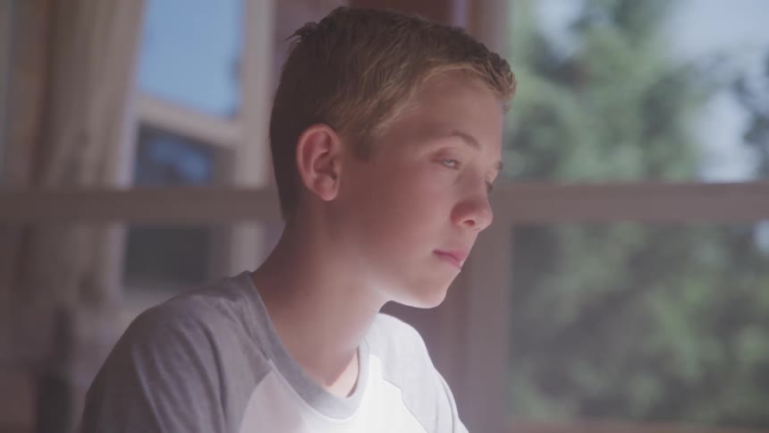 A white boy sits in a home and stares off into the distance