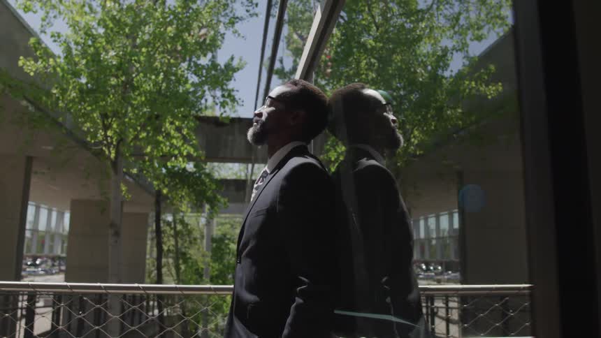A black man with suit standing in front of glass
