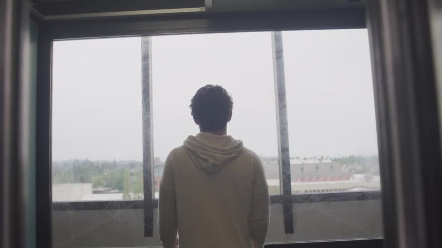 Man wearing a hoodie looks out the window while the elevators door closes in the building