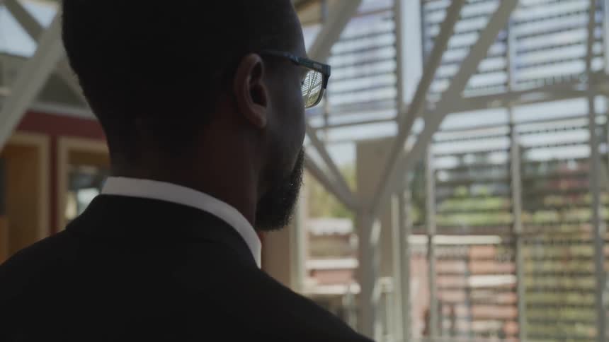 A man stands in an atrium and looks out the window