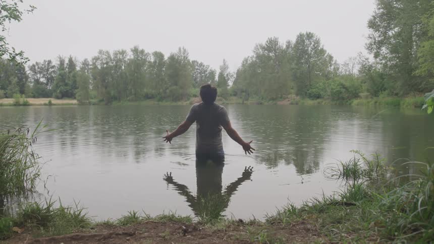 A man stands in lake in the rain surrounded by trees