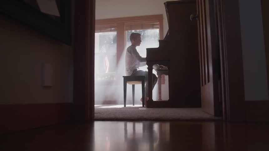 Boy plays the piano while the sun streams through the window in the room
