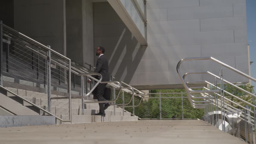 Black businessman wearing a suit and carrying a suitcase goes up the stairs