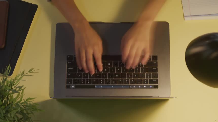 A persons hands typing on a laptop while sitting at a desk