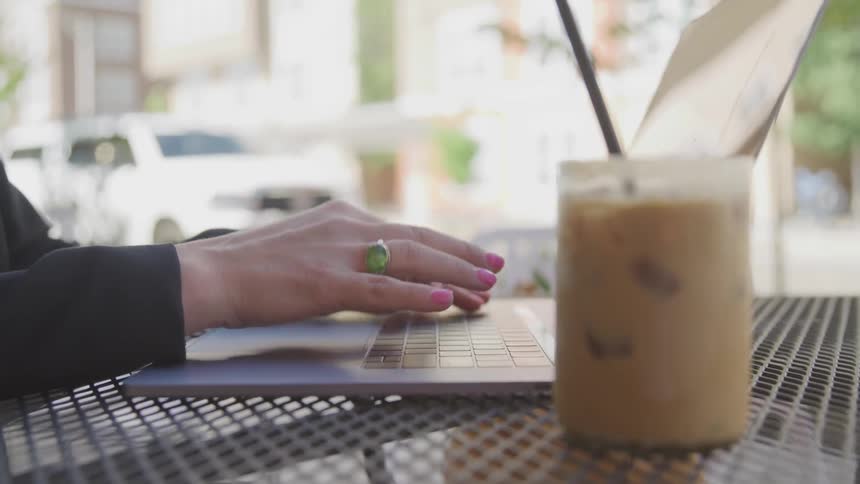 A woman types on her laptop with an iced coffee beside her