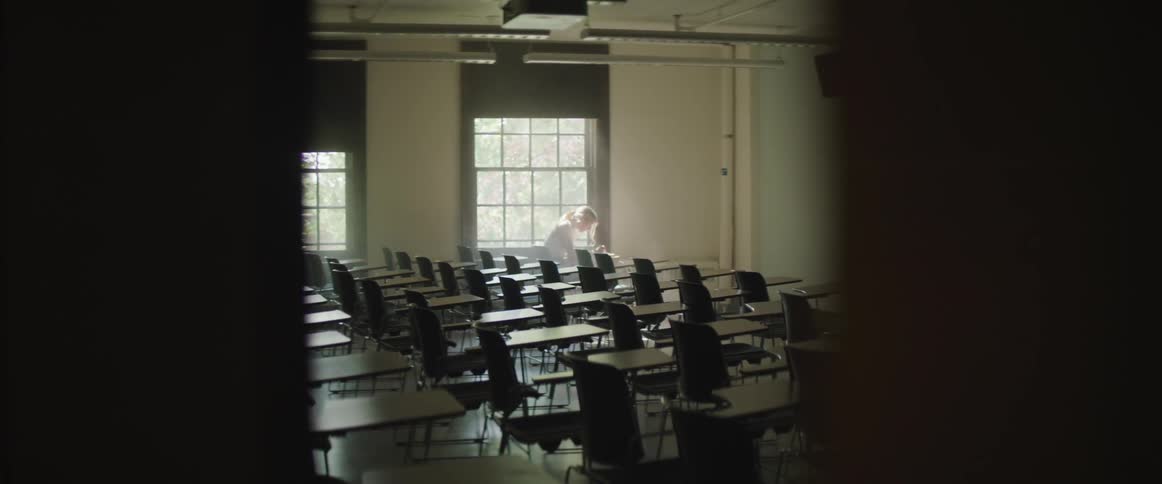 Blonde girl sits on the chair by the window in empty classroom