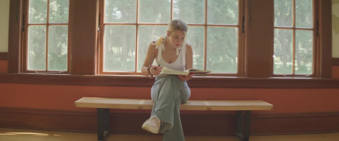 A woman sitting on a bench in front of a window reading a book