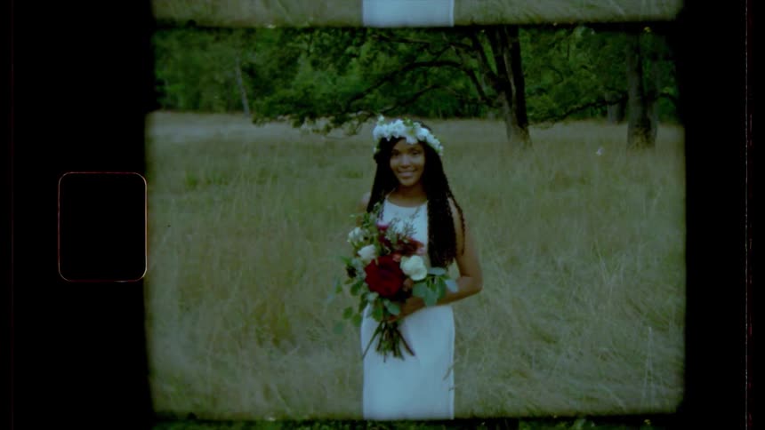 A woman stands in a meadow wearing a wedding gown and headpiece