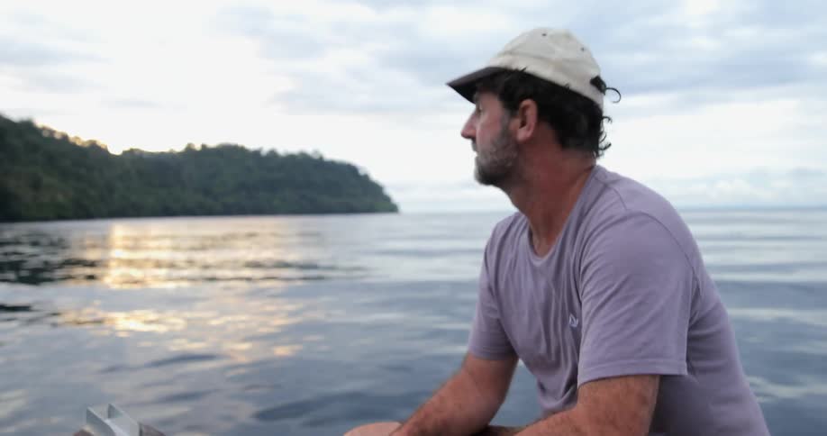 A man is sitting on a boat as it travels on a cloudy day