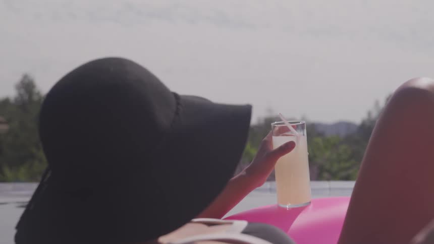 A woman holds on to a drink while floating in a pool