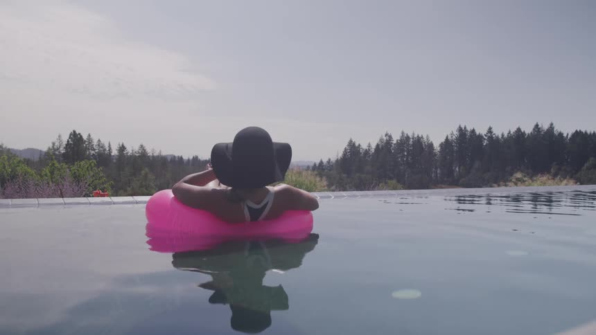 A woman relaxes while floating on an inflatable ring in an infinity pool