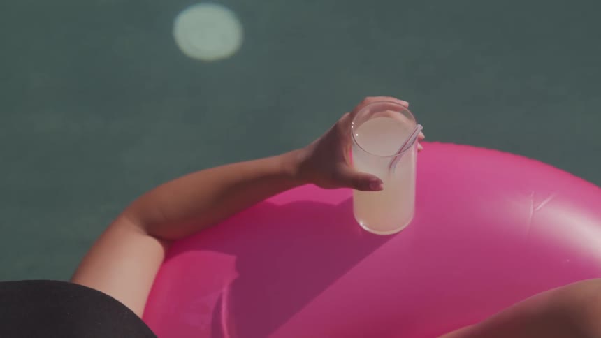 A woman relaxes with a drink while floating on an inflatable ring in an infinity pool