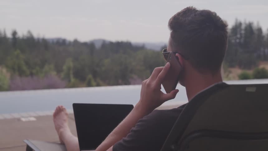 A man is talking on the phone and relaxing outdoors