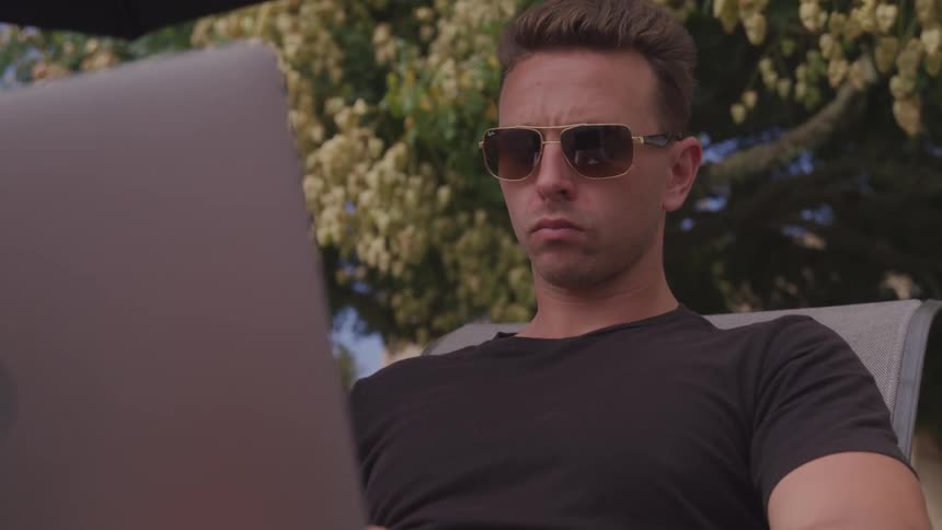 A young man sits outside and looks at his laptop
