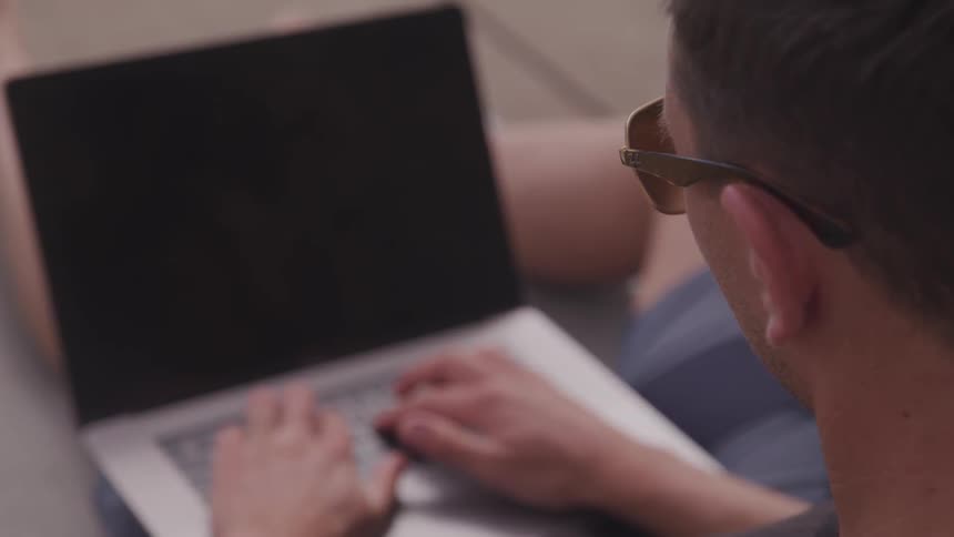 A man sits with legs outstretched working on a laptop